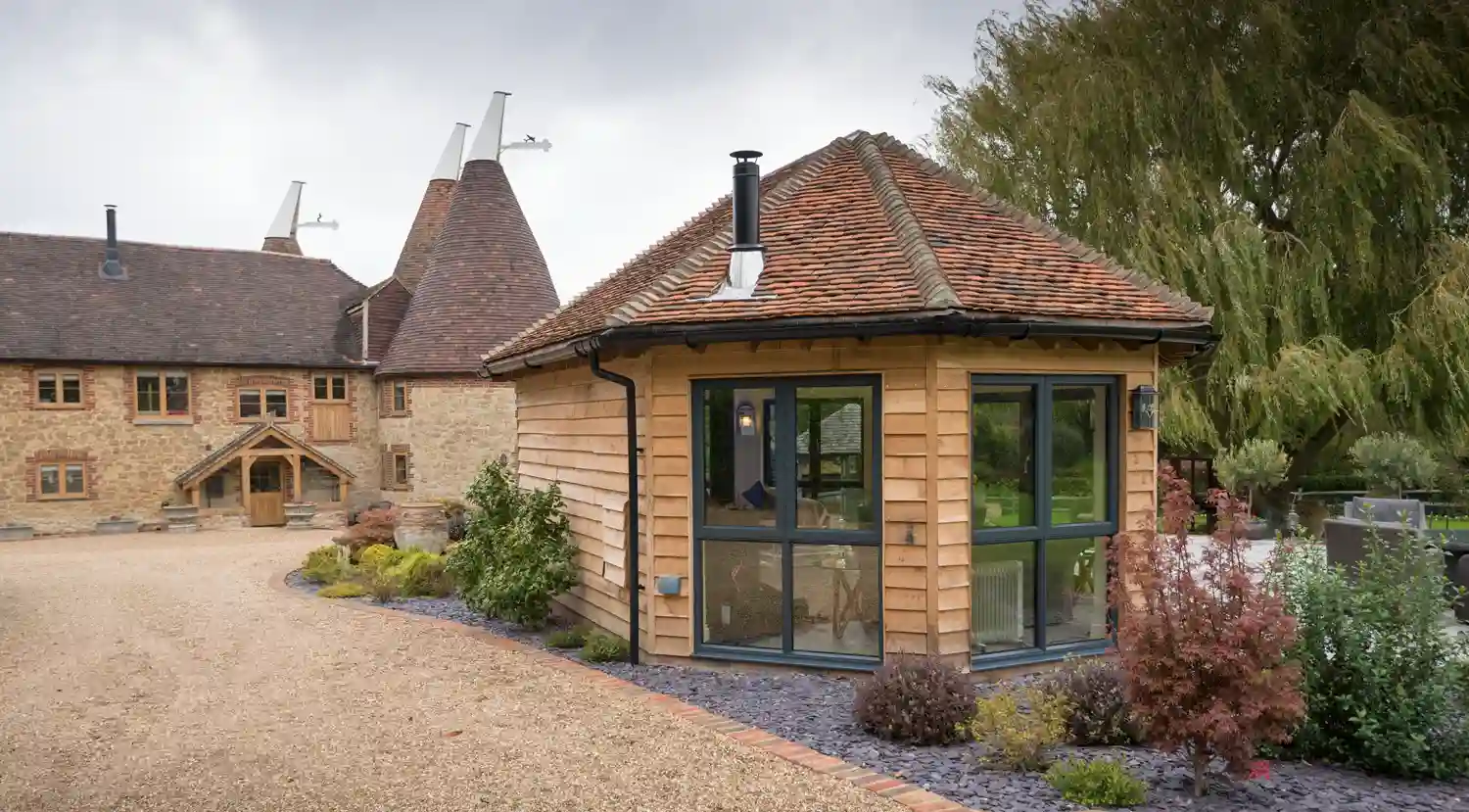A modern wooden extension with large glass windows sits next to a traditional stone building with conical roofs.