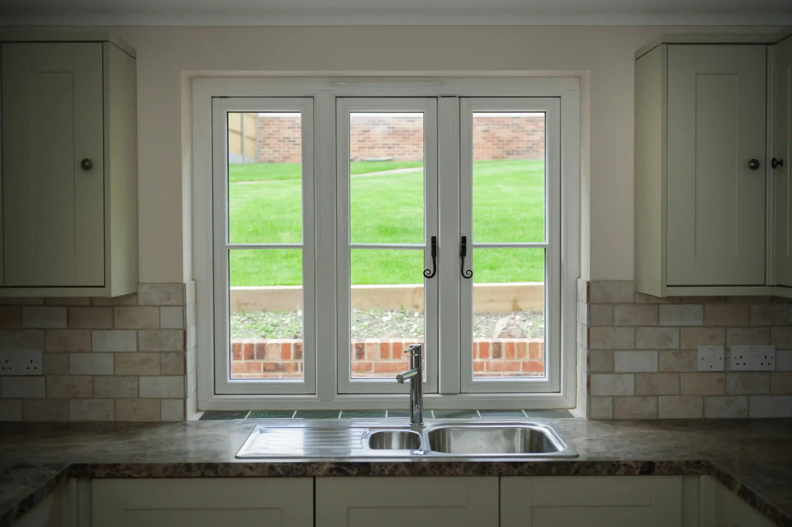 White uPVC French windows with garden view in kitchen with marble sink