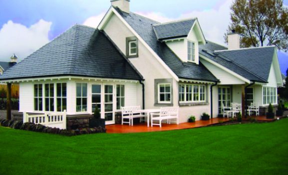 CWG Alan Brothers Sash Windows A white cottage with a dark grey slate roof and a wooden deck surrounded by a green lawn.