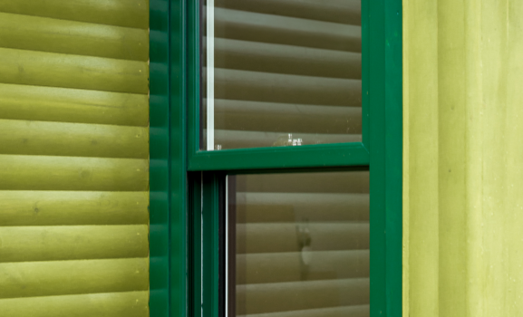Dual colour A green-framed window set into the light green wooden siding of a log cabin.