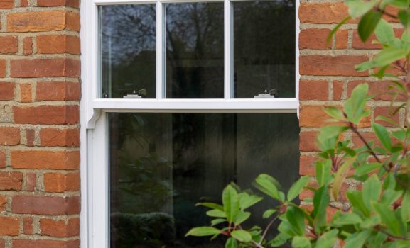 deep base rail A white sash window set in a red brick wall with green leaves in the foreground.