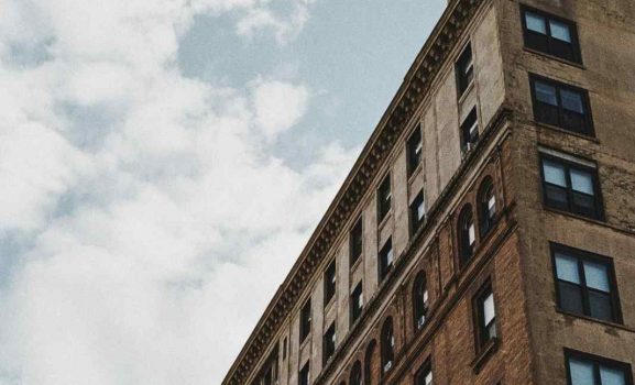 Tall building with numerous windows under cloudy sky.