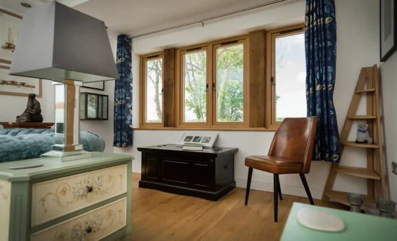 wooden img 2 A bright bedroom featuring a large window with wooden frames, blue patterned curtains, and a brown leather chair.